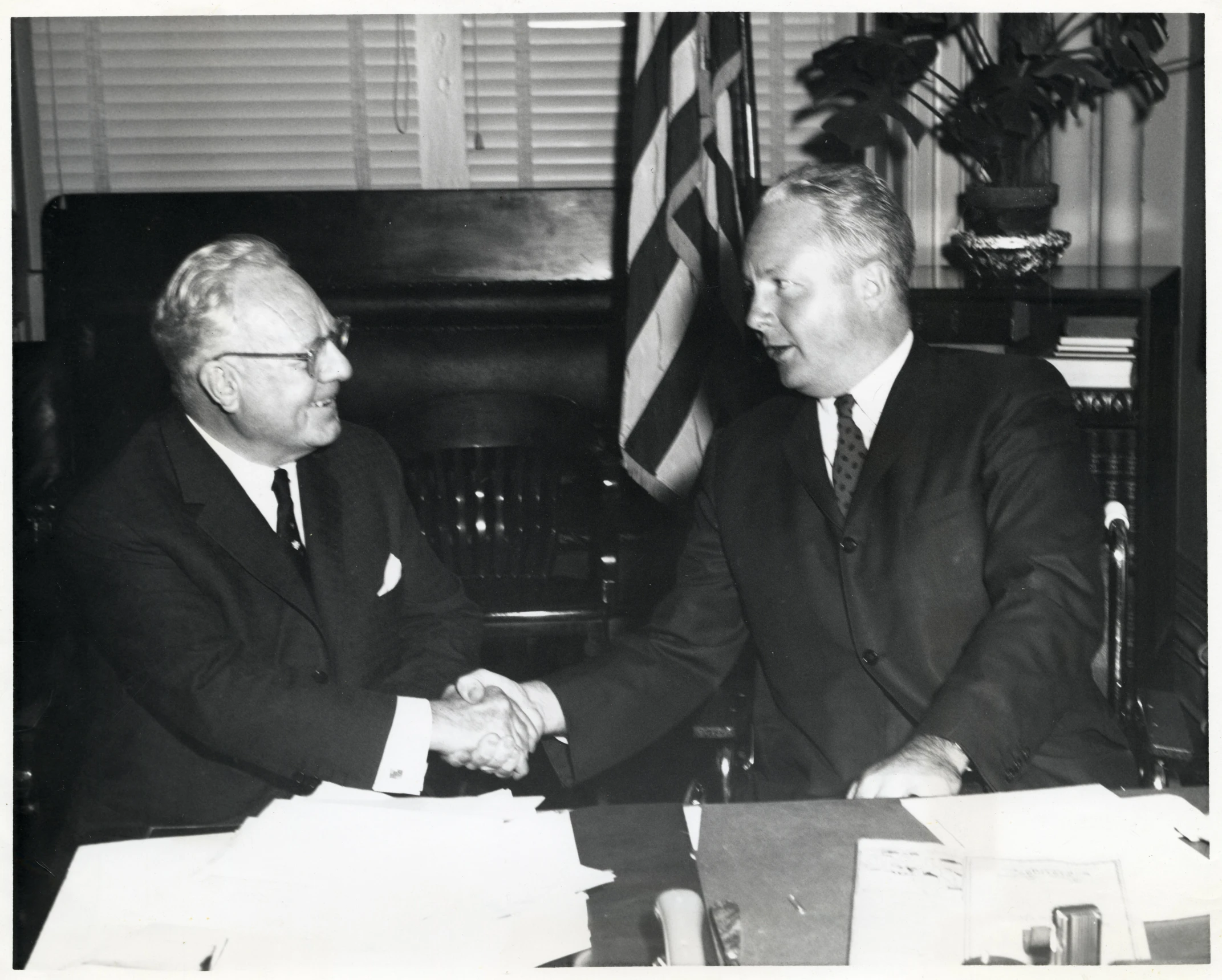 two men in suits shake hands at a table