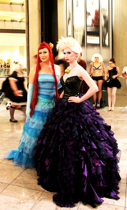 two woman with long hair and dressed in gowns stand near each other