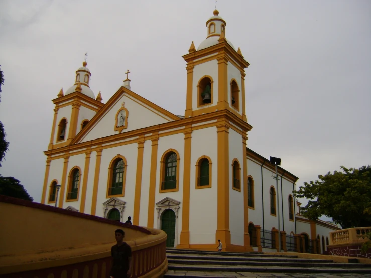 an old white and yellow church sitting on the side of a hill