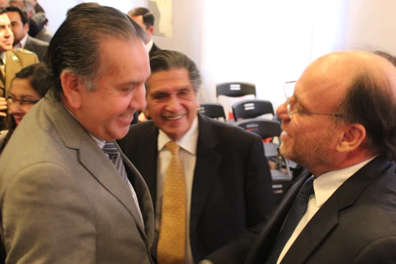 two men in suits standing close together with others in the background