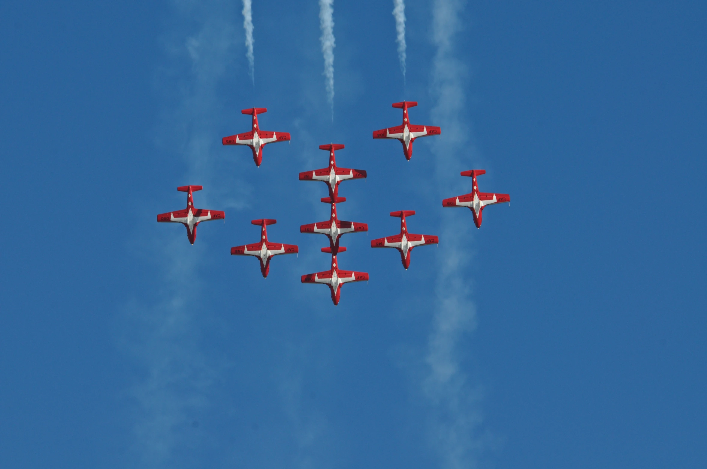 red and white planes flying in formation with smoke coming out