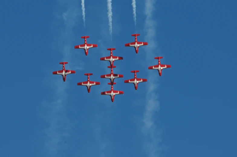 red and white planes flying in formation with smoke coming out