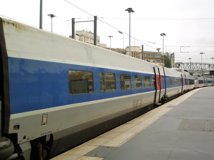 a very long blue and white train stopped by the side of a building