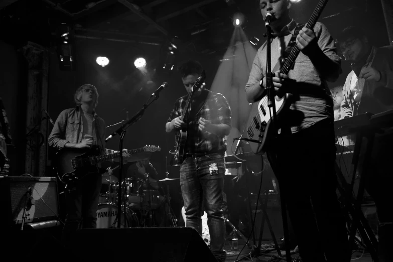 four men on stage with guitars and microphone