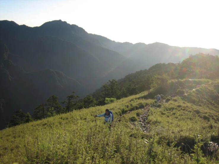 a couple of people hiking up a grass covered hill