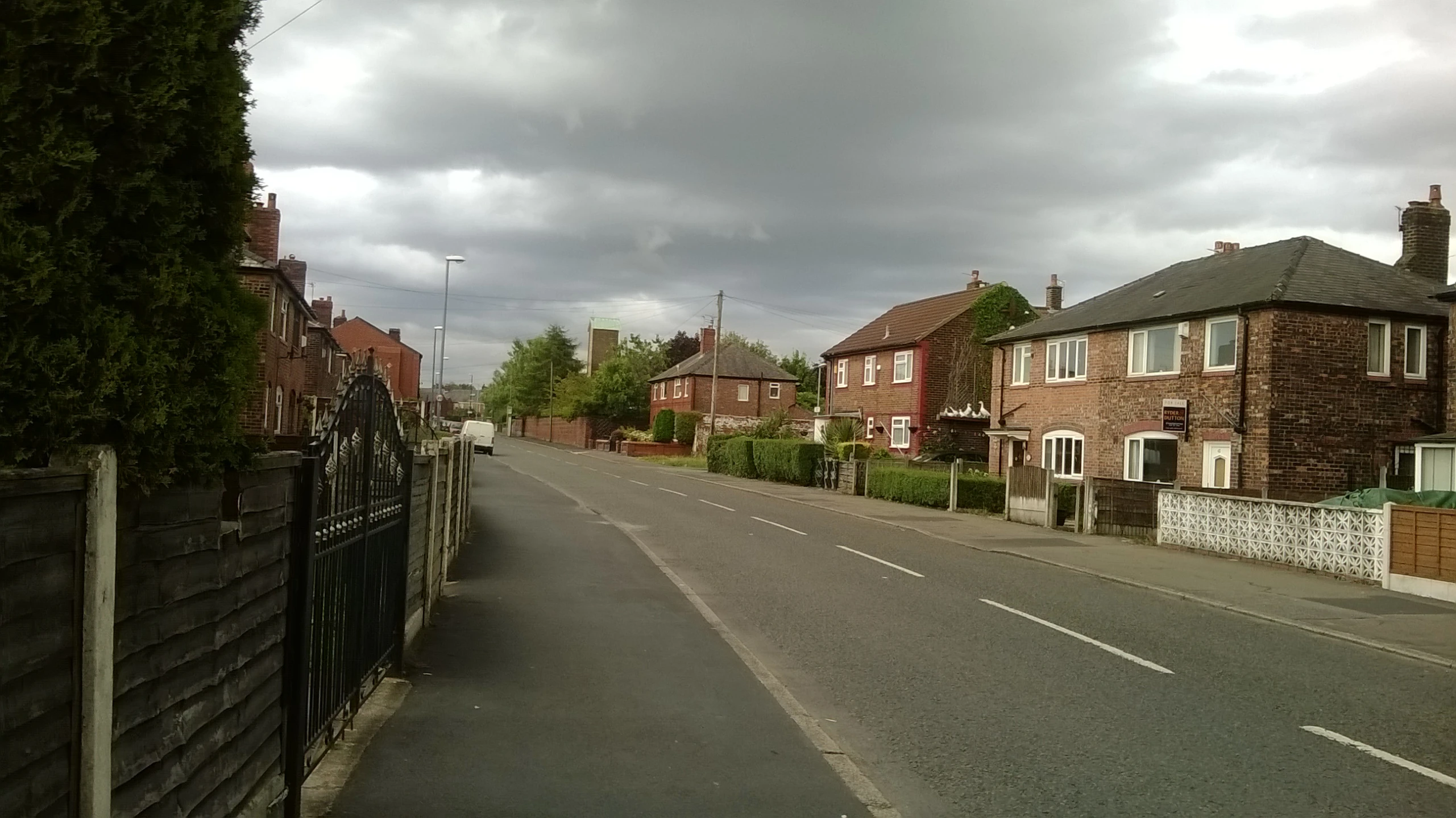 a view of a street with a house, fence, and a car in the road