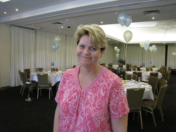 a woman wearing a pink top stands near the room filled with tables