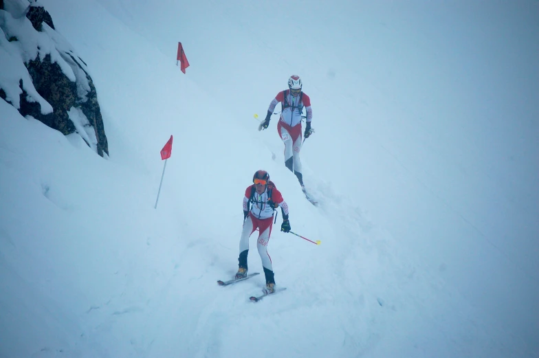 two men in ski gear skiing down a steep slope