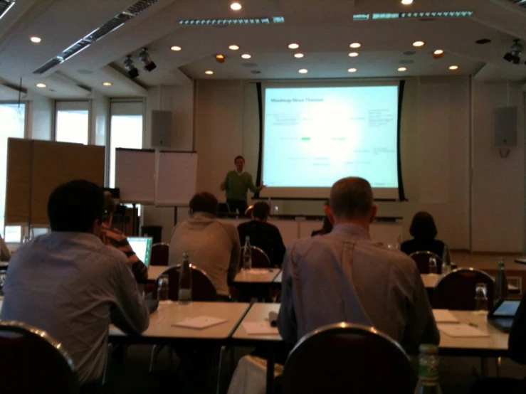 a group of people are sitting at tables watching an instructor on a projector