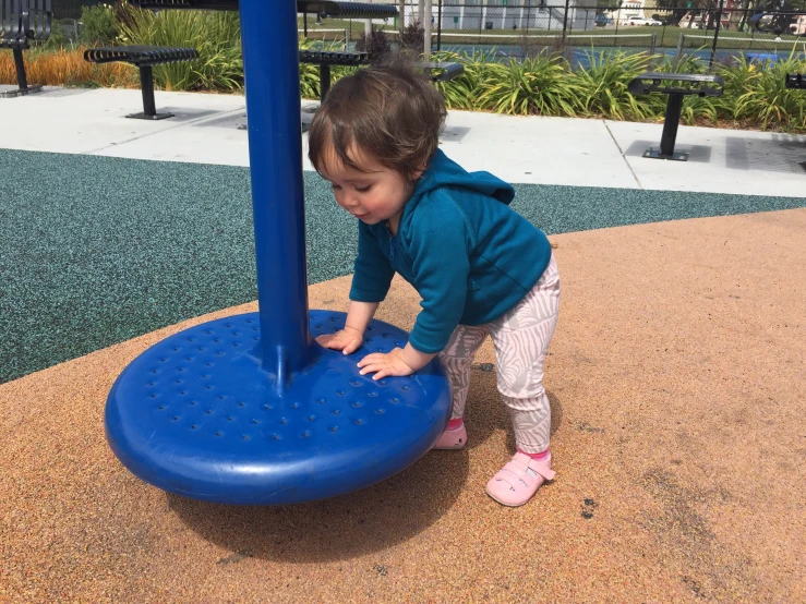 little girl climbing on blue circular thing in park