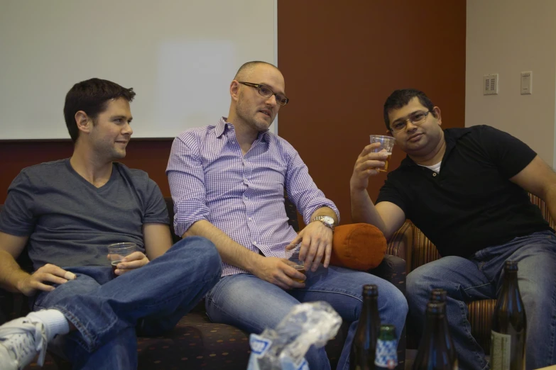 the men are drinking beer while talking on the couch