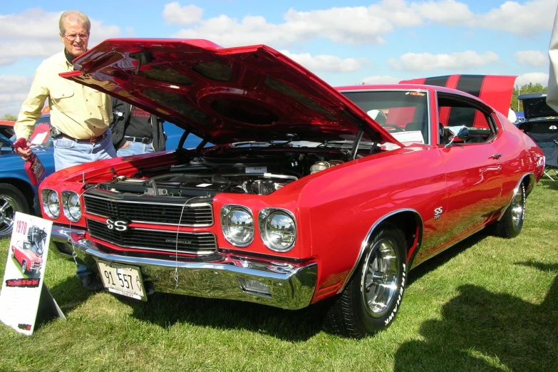 a man standing next to an old red car