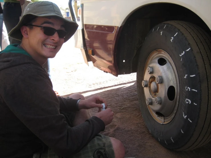 a man sits under a white bus with the tire in focus