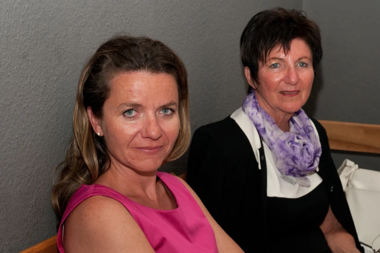 two woman sitting together in front of a wall