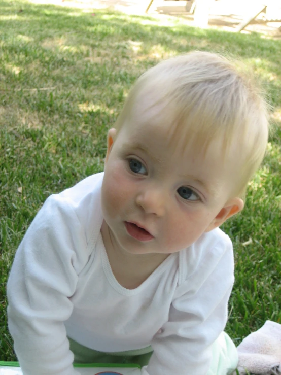 a baby sitting in the grass playing with a piece of broccoli