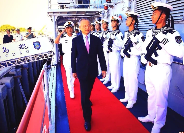 a man walking down a red carpet next to men in navy uniforms