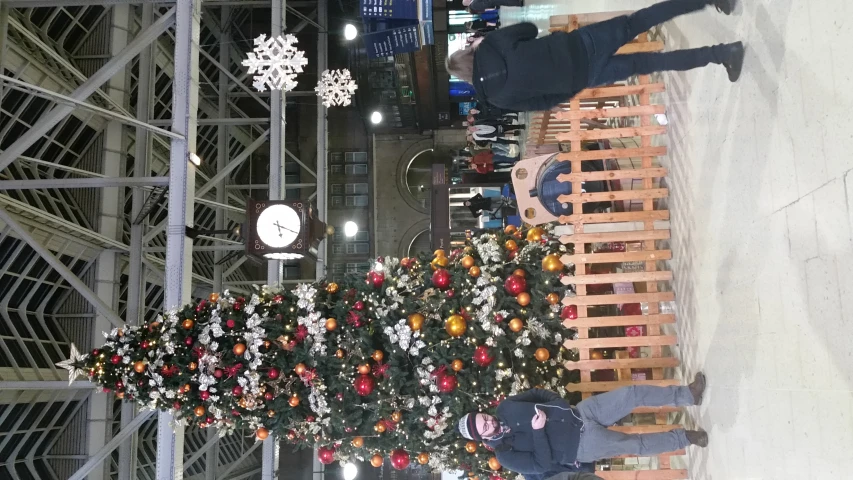 a large christmas tree and a man standing by a fence