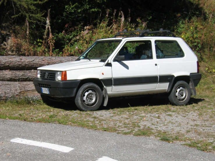 an old vehicle parked by a tree on the side of a road