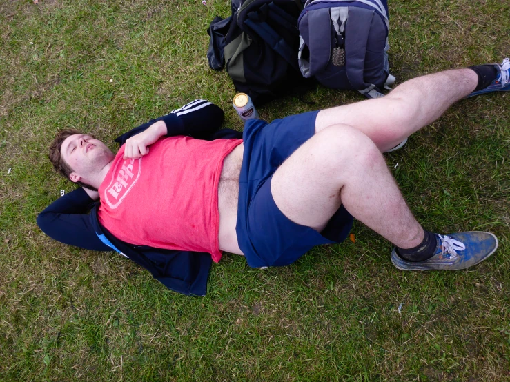 the man with glasses on lies in the grass near backpacks