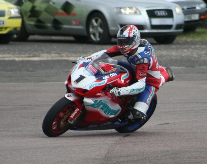 motorcycle racer turning corner of road next to two cars