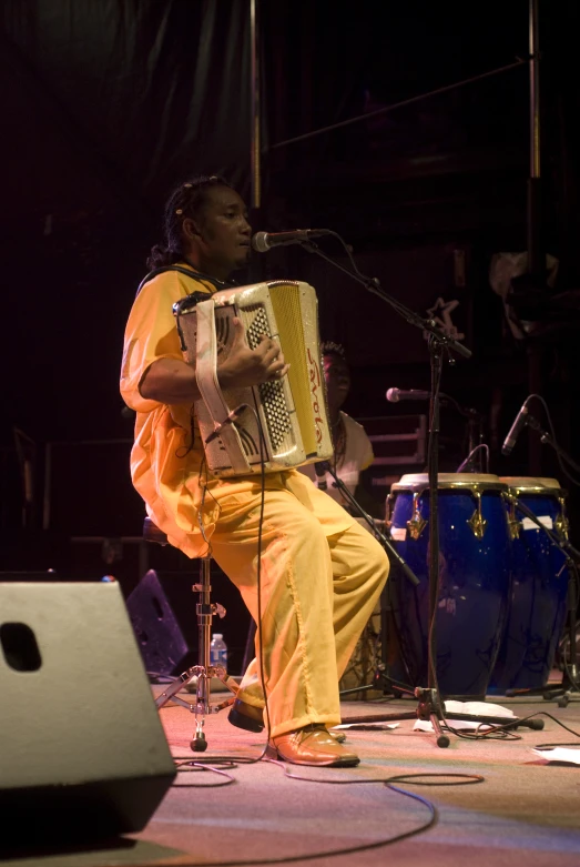 a man sits on a stool in front of a microphone and a music instrument