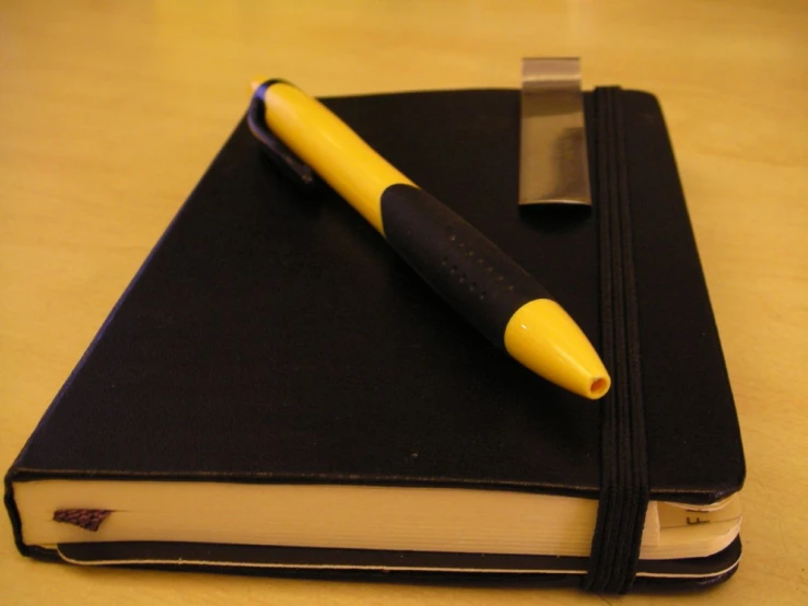 a yellow pen and book sitting on top of a wooden table