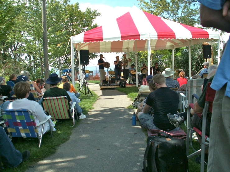 a tent set up for an outdoor concert with people sitting in chairs underneath it