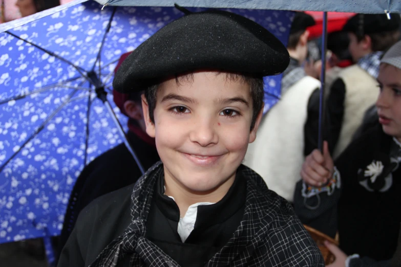 the boy in a hat smiles as he is holding an umbrella