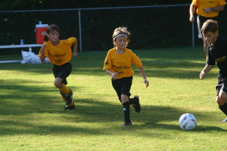 three children running towards a soccer ball on a soccer field