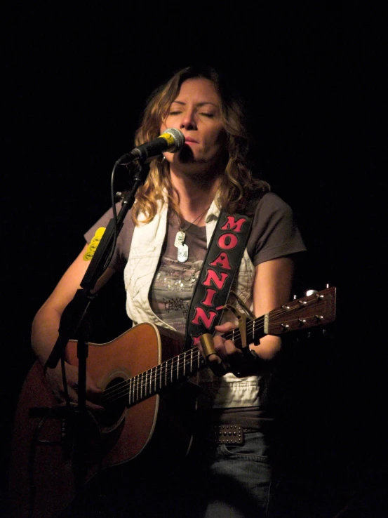 woman holding guitar and singing into a microphone