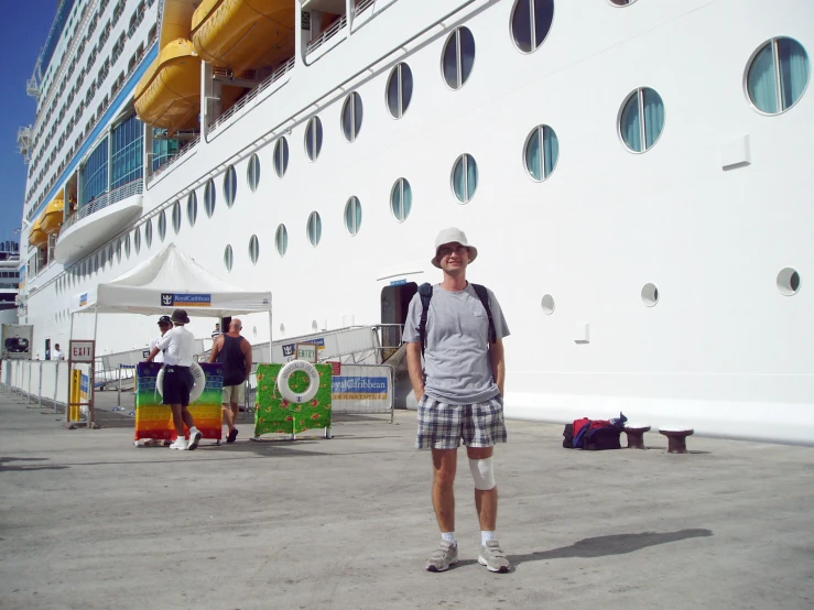 man in plaid shorts and tennis shorts posing in front of a cruise ship