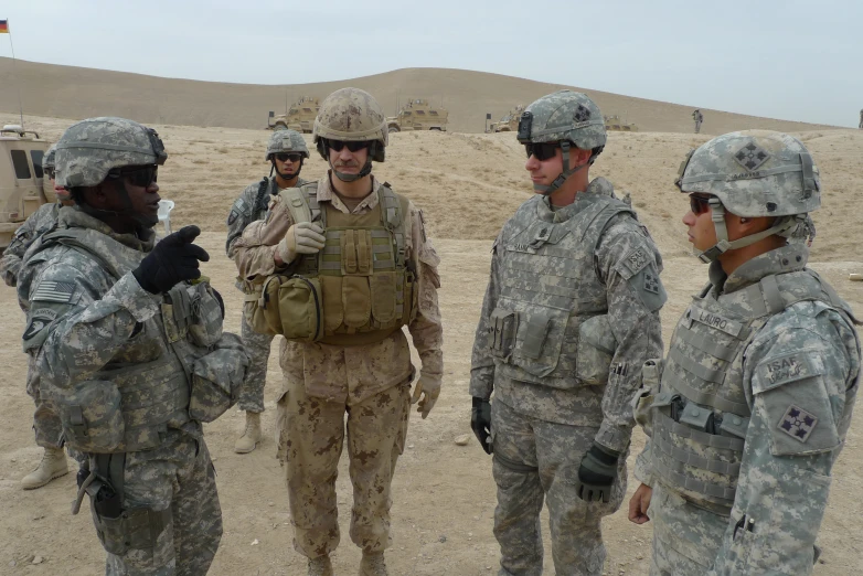 military personnel stand together in front of a desert