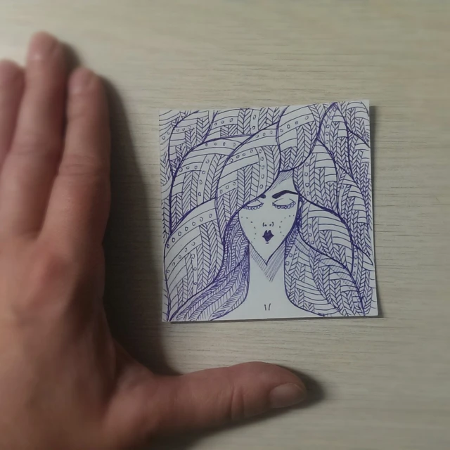 the hand is holding up an intricate illustration on a piece of paper