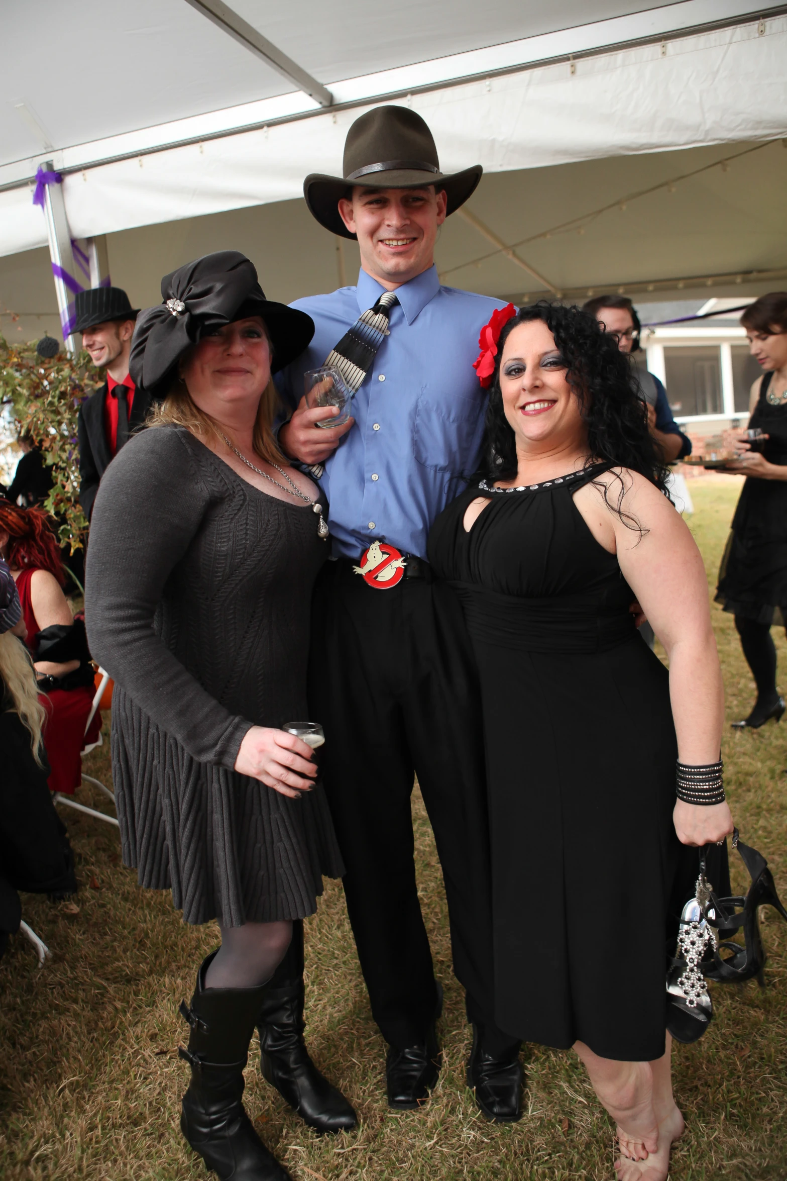 three people wearing black, dress clothes and boots, are standing together