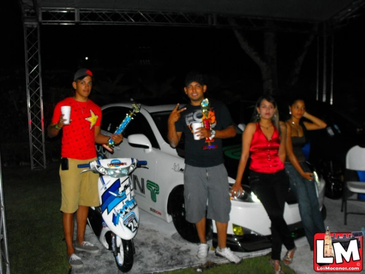 four people posing in front of a car while the car is parked