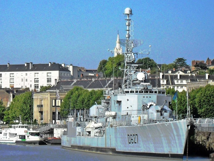 the large battleship is at the dock near some small boats