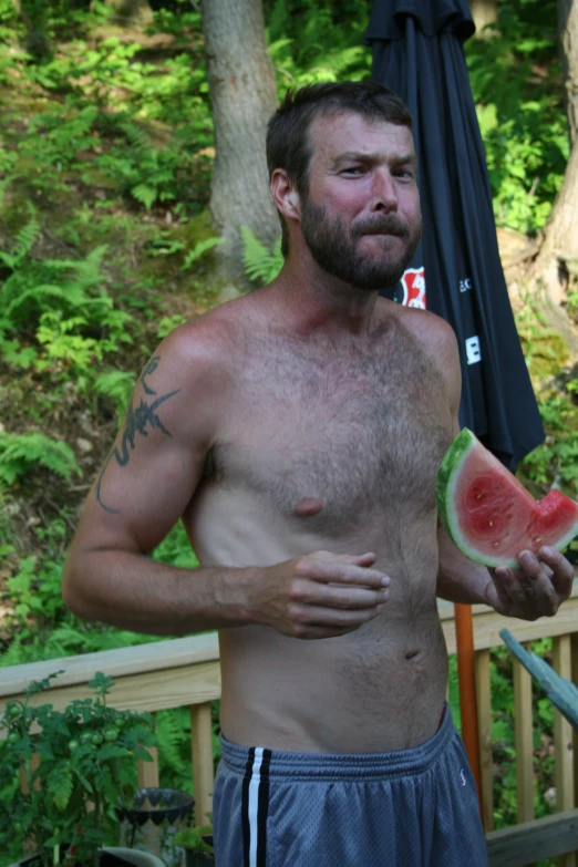shirtless man with beard eating a slice of watermelon