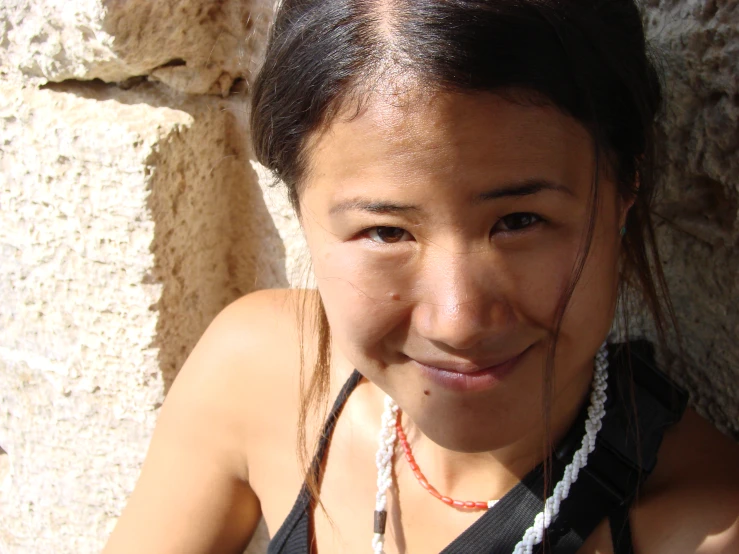 a woman with brown hair wearing a black top and pearls necklace