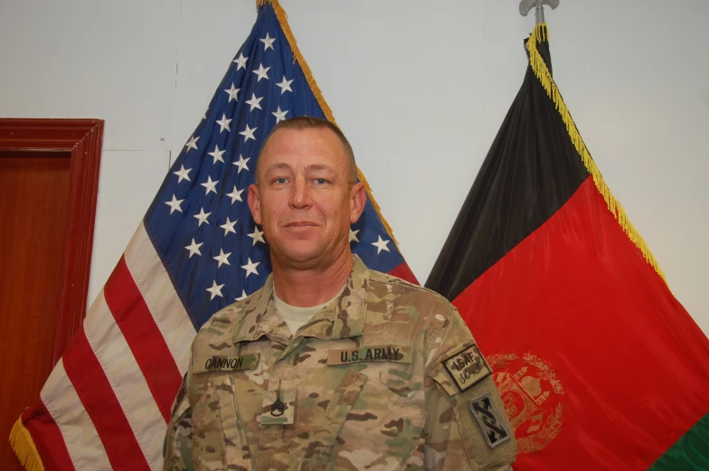 an official pograph of a man in camouflage posing in front of flags