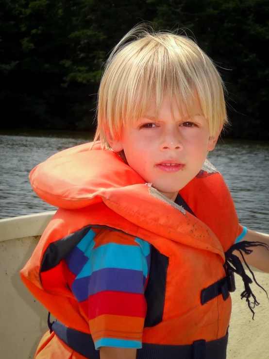 a boy with blonde hair and orange life jacket on