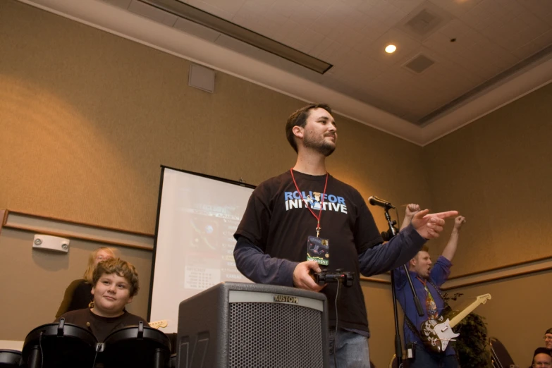 a man speaking on a stage next to a projector screen