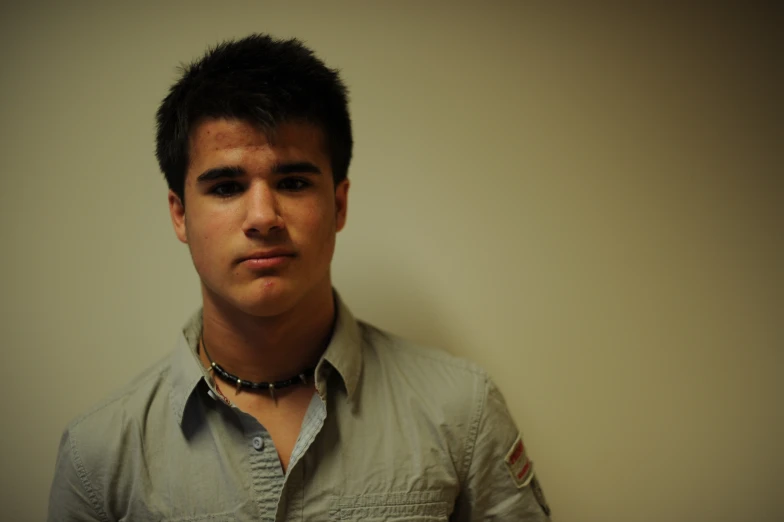 a guy is standing in front of a wall and wearing a necklace