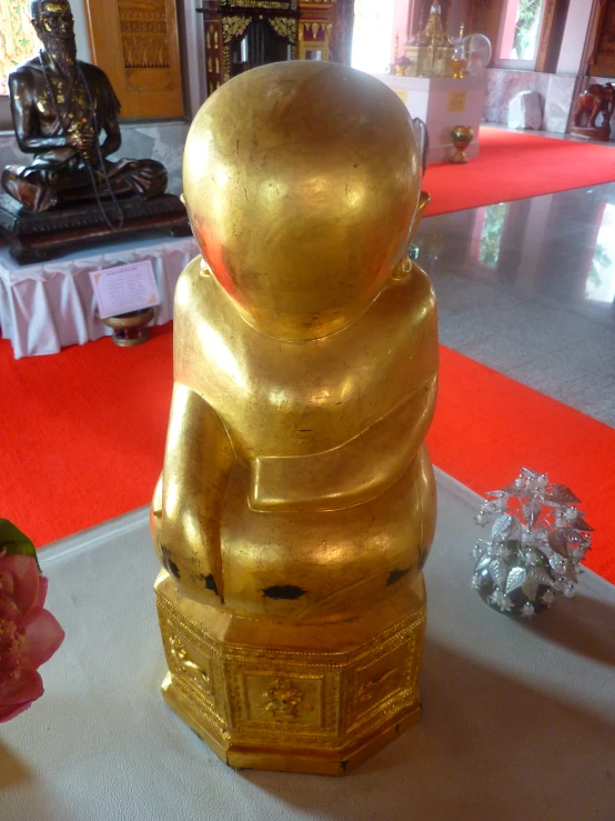 gold statue with two heads folded and on display in front of floral arrangement