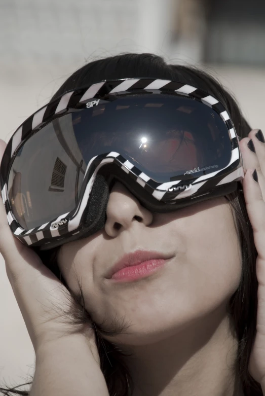 a woman holds a black goggles with a striped frame