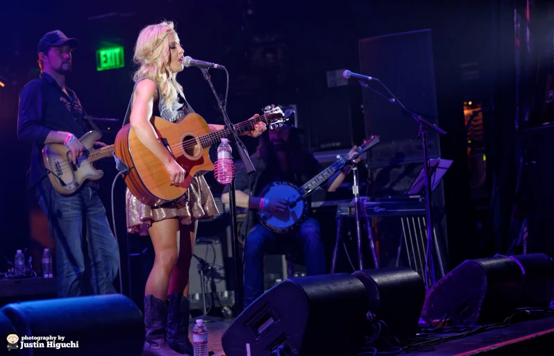 a woman standing on stage singing with an acoustic guitar