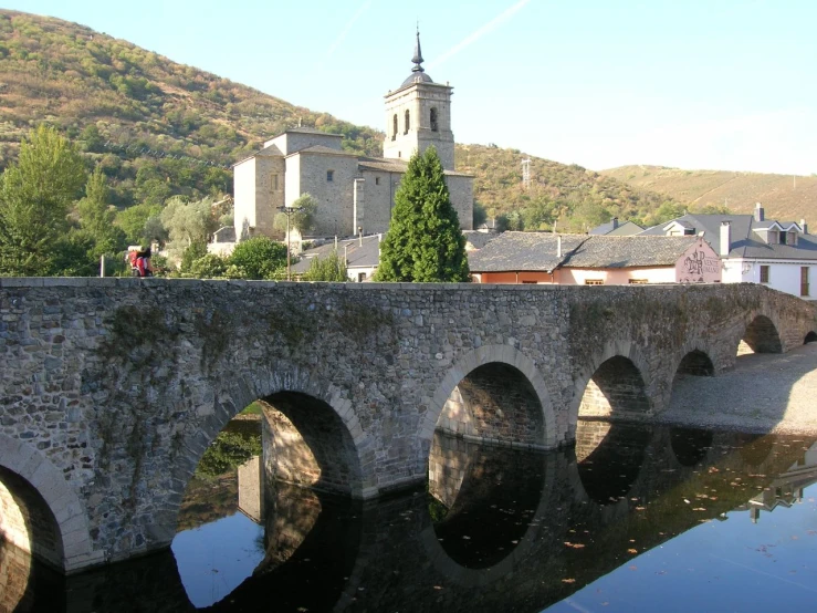 a stone bridge crosses across a river with buildings and towers in the background