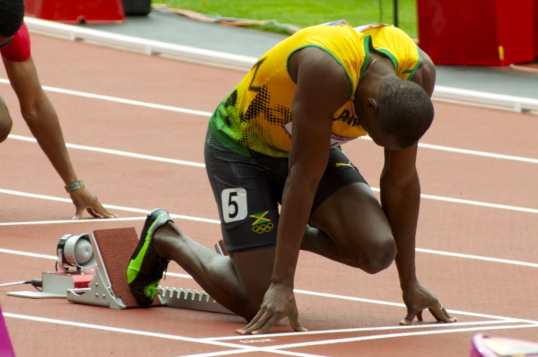 a male in a yellow and black shirt is crouched down on a track