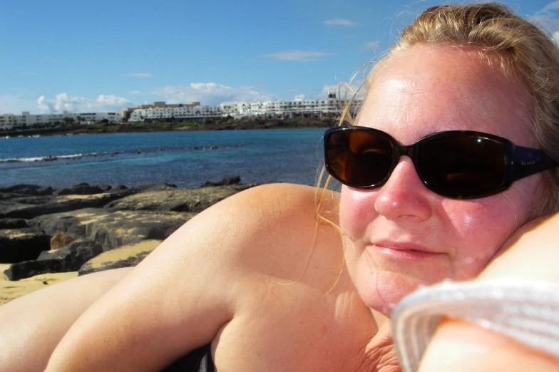 woman in sunglasses laying on the rocks next to the ocean