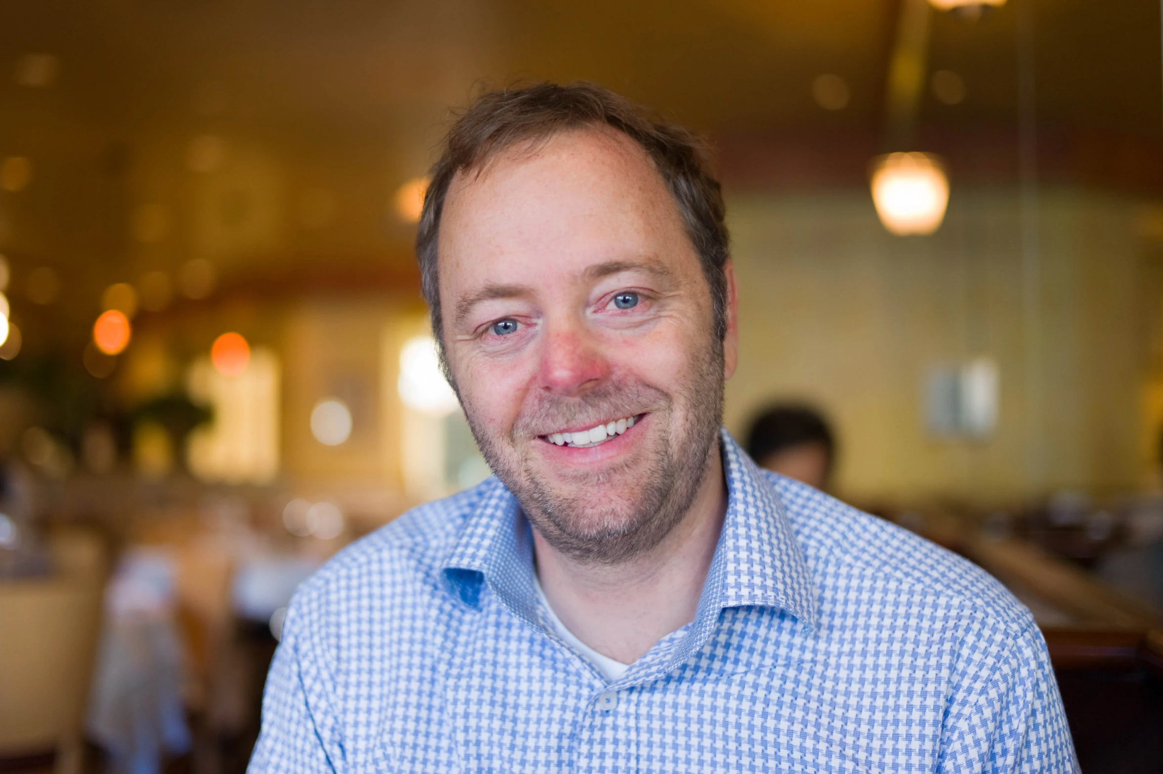 a man in blue and white checked shirt smiling