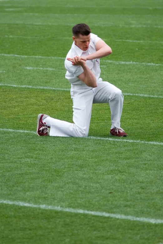 a young man in a baseball uniform standing with his hand on his hip while kneeling down